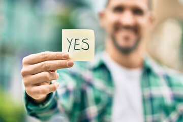 Poster - Young caucasian man smiling happy holding yes reminder papaer at the city.