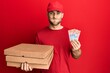© Krakenimages.com - Young caucasian man holding delivery box and swiss franc banknotes puffing cheeks with funny face. mouth inflated with air, catching air.