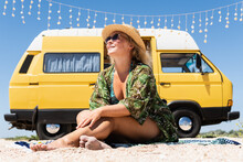 Young Blonde Woman Travelling By Vintage Campervan At The Seaside. Relaxing On The Beach.