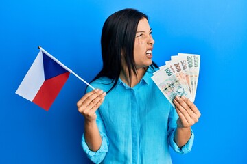 Sticker - Young latin woman holding czech republic flag and koruna banknotes angry and mad screaming frustrated and furious, shouting with anger. rage and aggressive concept.