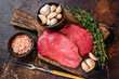 Raw rump beef meat steaks on butcher wooden board. Dark background. Top view
