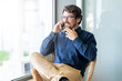 © Joao - Casual man wearing glasses talking on the phone. Successful male portrait sitting on a chair at the office by the window