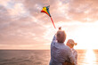 © Daniel - close up and portrait of two old and mature people playing and enjoying with a flaying kite at the beach with the sea at the background with sunset - active seniors having fun.