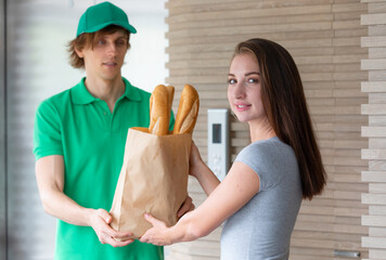 A young boy food delivery sender holding a grocery paper bag arrives at the customer's place and sends a paper bag for the client.