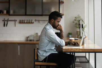 Wall Mural - Side shot of thoughtful african man student learning on distance by computer app pondering on test exam question. Pensive young black guy spend time at home using laptop search information in internet