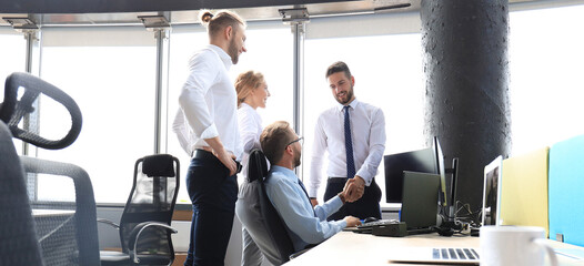 Poster - Two cheerful businessmen shaking hands while being in office together with their colleagues