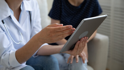 Wall Mural - Crop close up of woman doctor or nurse and patient use look at tablet screen discuss consider analysis results. Female GP and client hold pad device analyze treatment in clinic. Recovery concept.