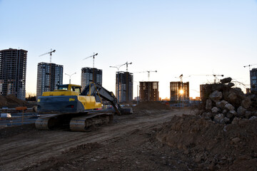 Wall Mural - Excavator on earthworks at construction site. Backhoe on foundation work and road construction. Tower cranes in action on blue sky background. Heavy machinery and construction equipment