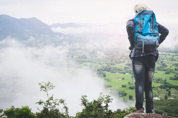 Wall Mural - Success african man traveler standing on the top of mountain with misty foggy landscape