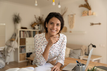 Wall Mural - Portrait of smiling young Caucasian woman study online on laptop making notes. Happy millennial female take distant course or training on computer, work on internet on gadget from home office.