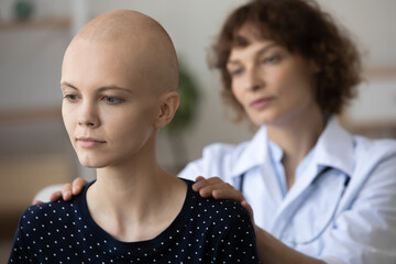 Wall Mural - Caring female nurse or caregiver touch support young Caucasian hairless female cancer patient in clinic. Attentive doctor comfort feel supportive to thoughtful bald woman struggle with oncology.