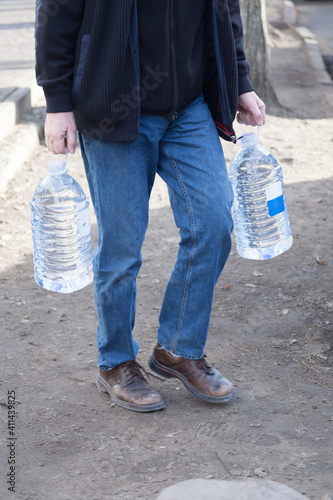 The man carries two bottles of drinking water. © indigolotos