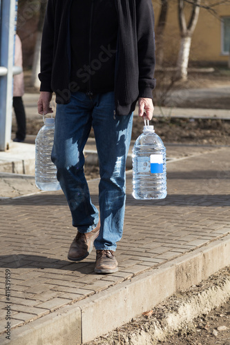 The man carries two bottles of drinking water. © indigolotos