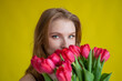 © Михаил Решетников - Woman with a bouquet of red tulips on a yellow background. Happy girl in a black dress holds an armful of flowers . Gift for Valentine's Day. The most romantic day of the year.