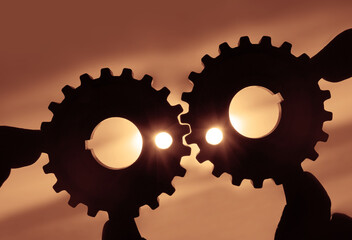 human hand holding two metal cog gear wheel on sunny sky background. sunshine and yellow sky . sun rays. one part of whole. symbol of association and connection. silhouette of iron cogwheel