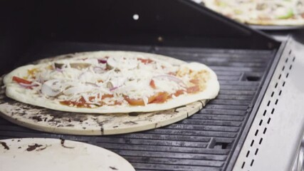 Wall Mural - Preparing individual grilled pizzas on an outdoor gas grill.