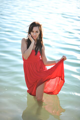 Wall Mural - Beautiful young woman in long red dress running on a tropical beach. Blue sea on the background.