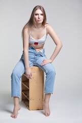 Female in underwear sits on a wooden box on gray background.