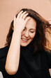 © zzzdim - Painfully smiling middle aged woman trying to untangle hair strand with fingers. Eyes closed. She has subtle cat eye makeup, she wears black shirt