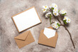 © Yulia - Blank wedding card mockup in brown envelopes and cherry blossom branch (artificial). Beige grunge background. Spring stationery still life. Top view, flat lay.