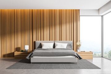 Corner of master bedroom with wooden walls, panoramic window with countryside view, comfortable king size bed standing on gray carpet and concrete floor.