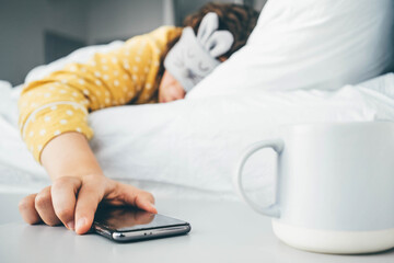 Woman in sleeping mask being woken by mobile phone In bedroom.