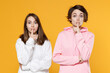 © ViDi Studio - Secret two young women friends 20s wearing casual white pink hoodies standing saying hush be quiet with finger on lips shhh gesture isolated on bright yellow color wall background studio portrait.