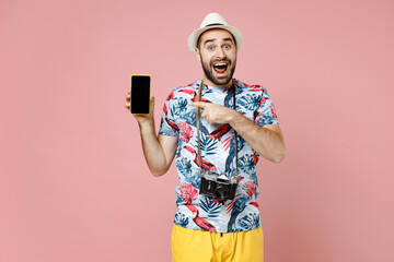 Shocked young traveler tourist man in hat pointing index finger on mobile phone with blank empty screen isolated on pink background. Passenger traveling abroad on weekends. Air flight journey concept.