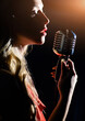 Sensual woman with red lips sings into a microphone. The singer records the song in a professional studio