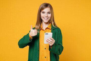 Wall Mural - Little blonde kid girl 12-13 years old in casual clothes green shirt hold mobile cell phone show thumb up gesture isolated on yellow background children studio portrait. Childhood lifestyle concept