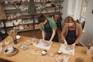 High angle portrait of two young people shaping clay while making ceramic bowls in pottery workshop, hobby and small business concept, copy space