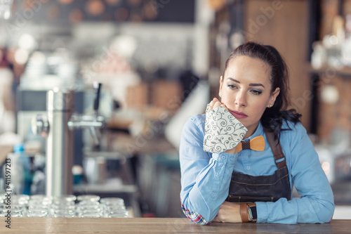 Sad female business owner holds face mask in her hand and leans against the bar in her empty cafe © weyo