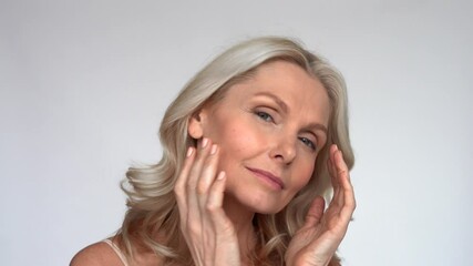 happy 50s middle aged mature woman touching facial skin looking at camera pampering in mirror. old h