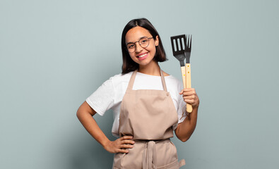 young hispanic woman smiling happily with a hand on hip and confident, positive, proud and friendly attitude