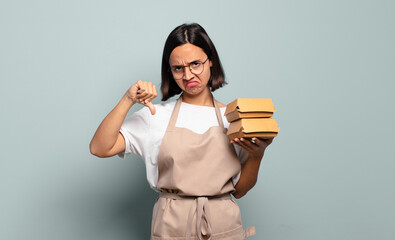 Wall Mural - young hispanic woman feeling cross, angry, annoyed, disappointed or displeased, showing thumbs down with a serious look