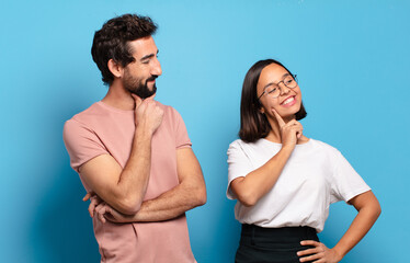 Canvas Print - young couple smiling happily and daydreaming or doubting, looking to the side