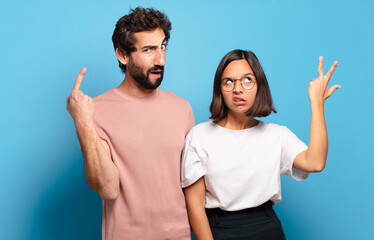 Wall Mural - young couple feeling confused and puzzled, showing you are insane, crazy or out of your mind