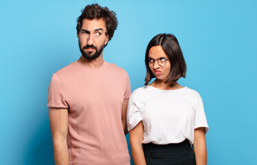 Wall Mural - young couple feeling sad, upset or angry and looking to the side with a negative attitude, frowning in disagreement