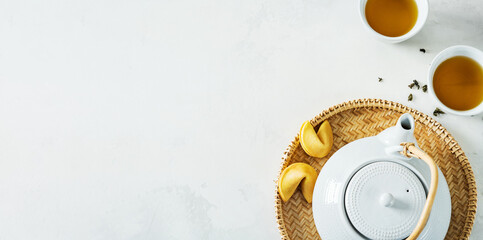 Wall Mural - Asian tea concept, two white cups of tea and teapot surrounded with green tea dry leaves view from above, space for a text on white background