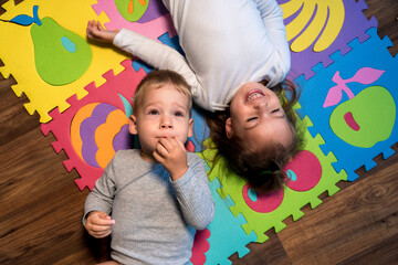 childhood, family friendship, games - close up portrait Two funny joy happy smiling little toddler peschool kids siblings twins brother with sister have fun lie playing on puzzles mat at home indoors