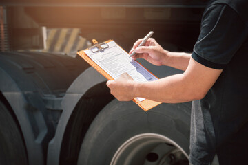 Truck driver holding clipboard his inspecting daily checklist safety of a truck wheels and tires. truck inspection and maintenance.