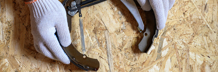 Wall Mural - men's hands in gloved are holds car drum brake disassembled on a sheet of osb plywood background. flat lay, top view. banner