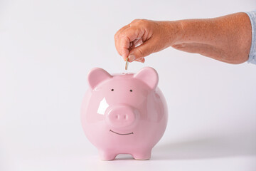 Hand of senior woman putting coin into piggy bank on light background. Concept of pension