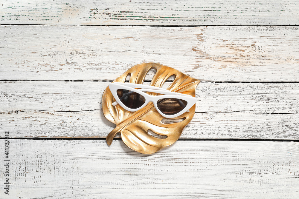Stylish sunglasses and golden leaf on wooden background
