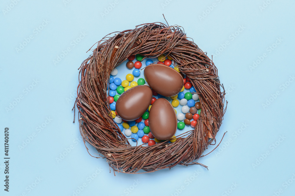 Nest with sweet chocolate eggs and candies on color background