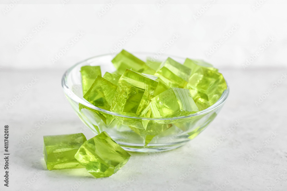 Glass bowl with tasty jelly cubes on light background