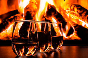 A beautiful glass with a drink near the fireplace. Firewood and fire. Glass and liquid.