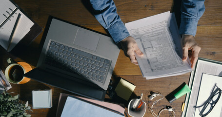 Wall Mural - Office worker checking paperwork and using a laptop