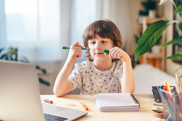 Wall Mural - Distance learning online education. Caucasian smile kid boy studying at home with laptop and doing school homework. Thinking child siting at table with notebook. Back to school.