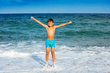 Portrait Of A Happy Relaxed Boy In Sunglasses With Big Smile Lift Hands Jumping In The Sea Waves